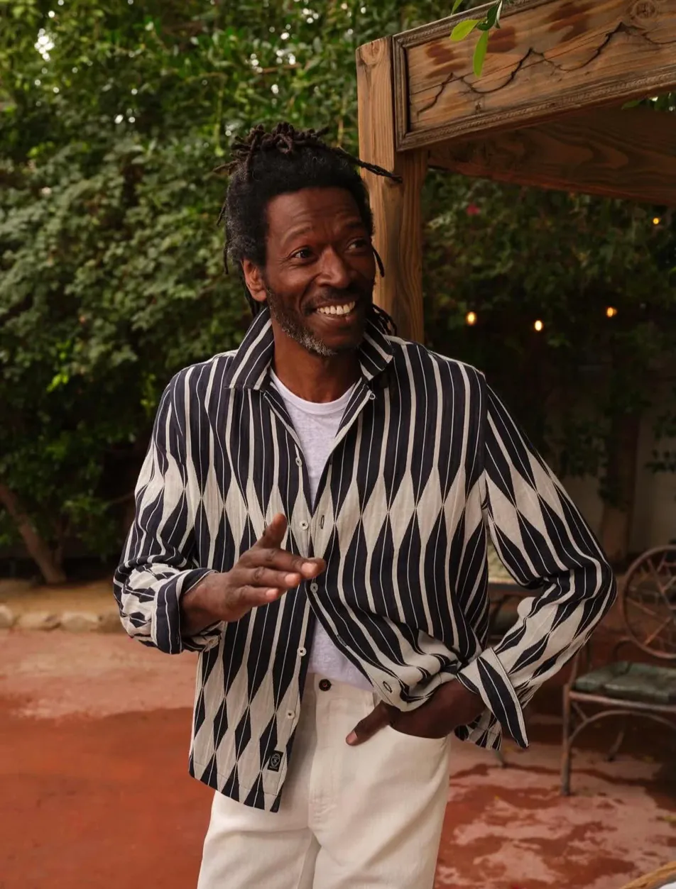 Image showing smiling Black man in black and white striped shirt gesturing outdoors with string lights